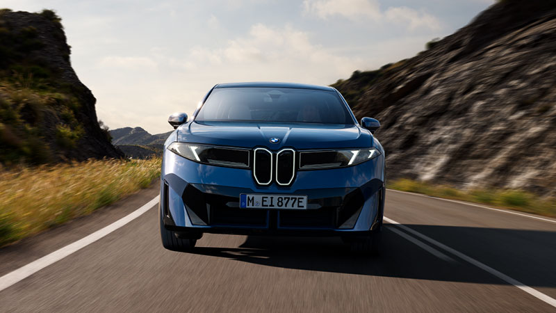 Vediamo una BMW iX3 blu in corsa su una strada panoramica