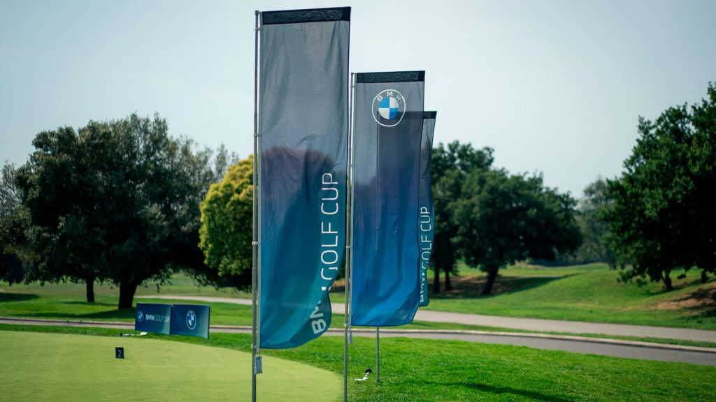 Vediamo tre bandiere con logo e scritta BMW Golf Cup su un campo da golf in una giornata di sole