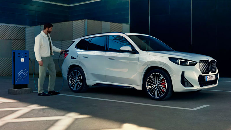 Vediamo un uomo che collega una BMW iX1 bianca ad una colonna per la ricarica elettrica