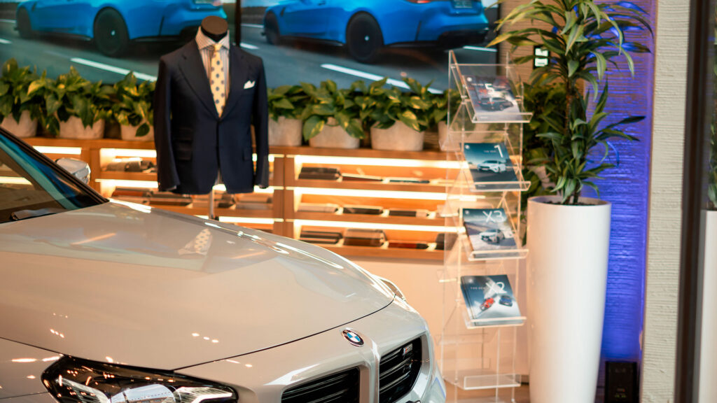 Showroom BMW con auto in esposizione, abito elegante e materiale promozionale