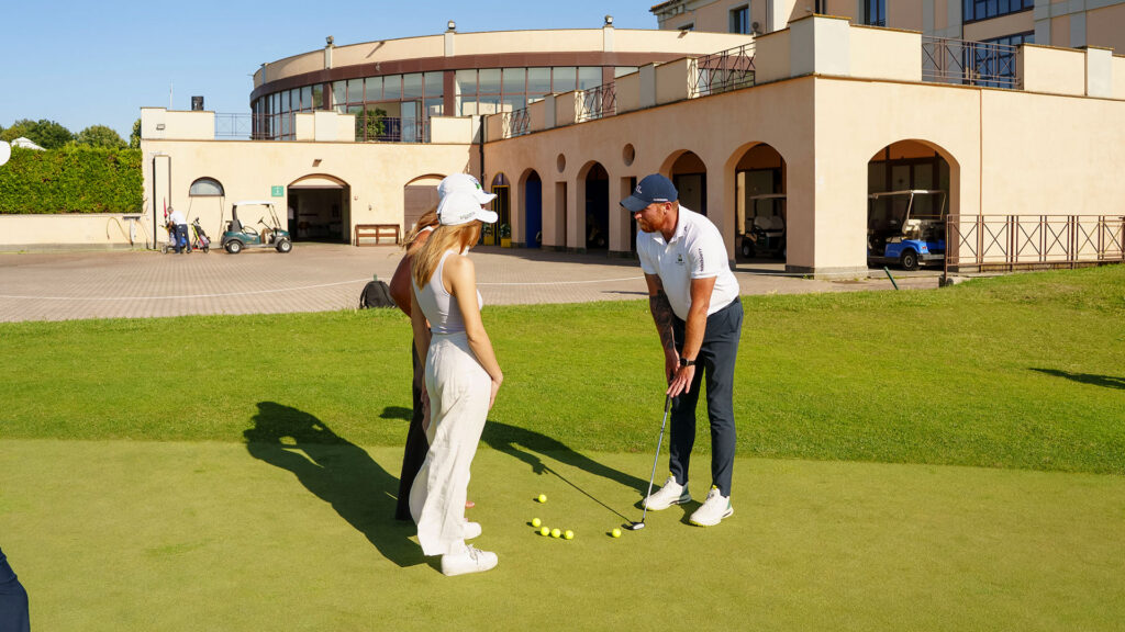 Vediamo un maestro che dà una lezione di golf su un green.
