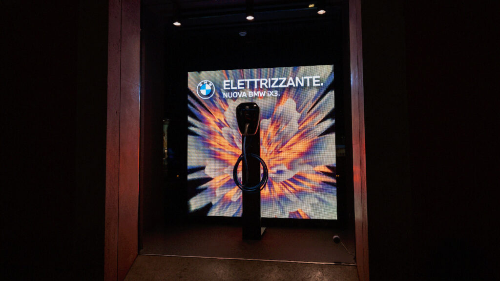 Una colonnina di ricarica BMW davanti a uno schermo luminoso con grafica esplosiva.