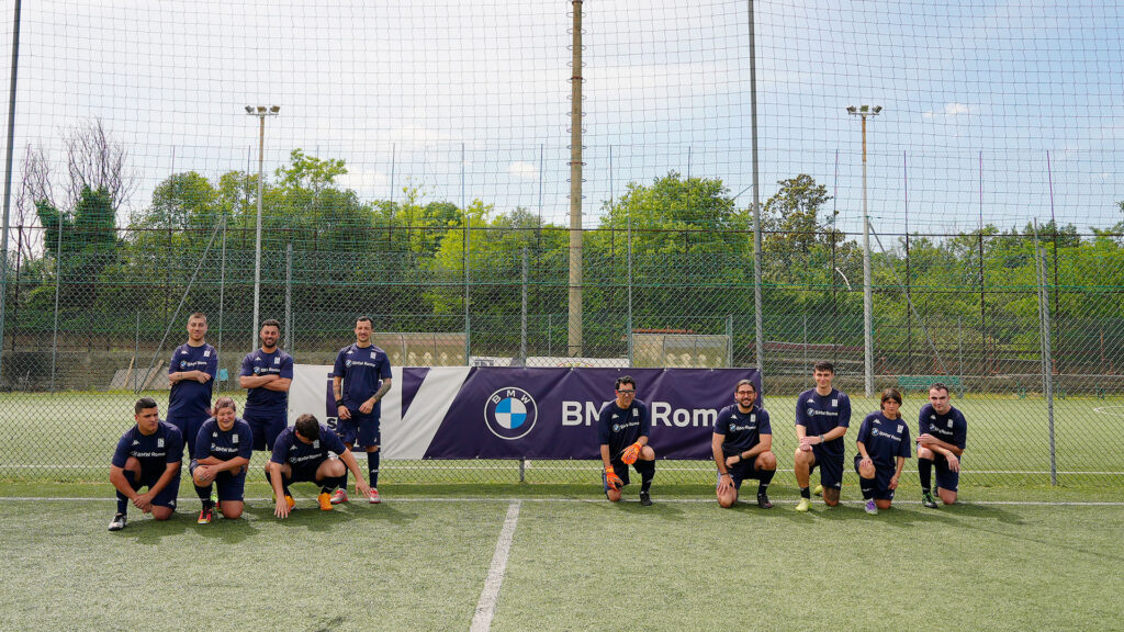 Vediamo una squadra in maglia blu che posa davanti allo striscione BMW Roma