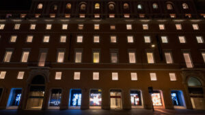 La facciata illuminata del palazzo Rinascente di notte con vetrine colorate.