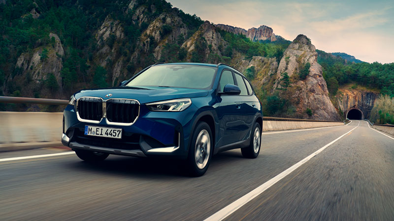 Vediamo una BMW X1 blu in viaggio su una strada panoramica tra le montagne